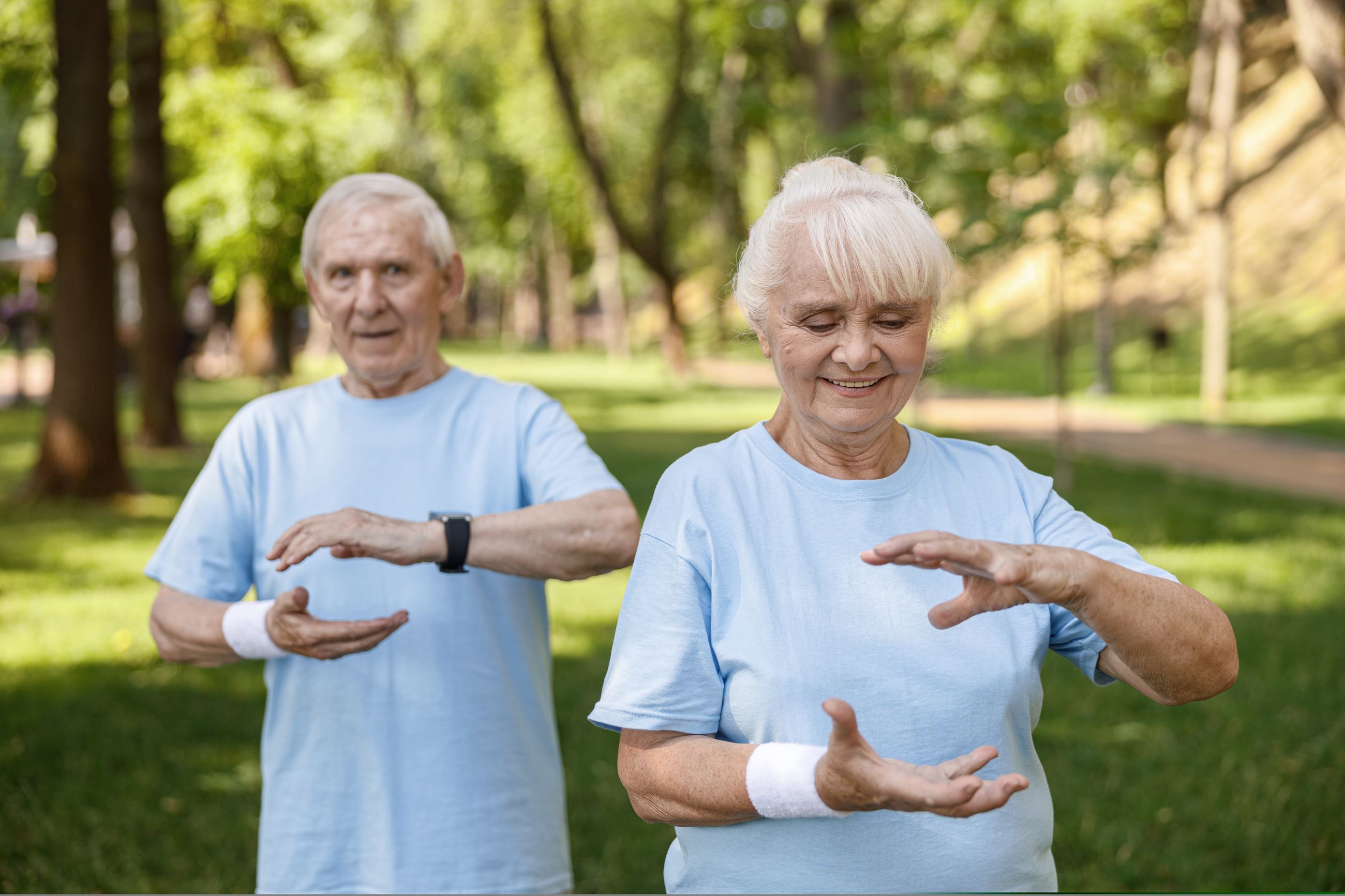 positive senior lady and man in sports clothes practice qigong together in park
